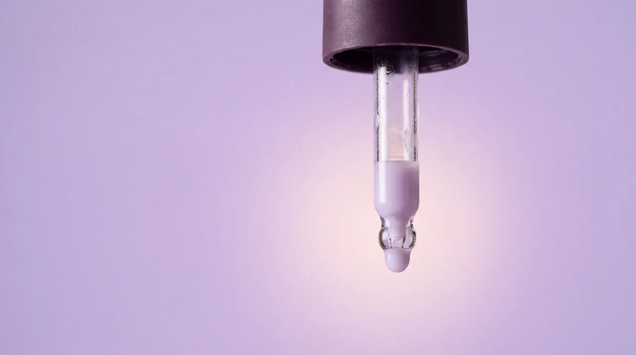 A drop of lilac serum forming at the tip of a glass dropper